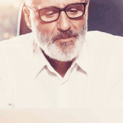 Unternehmenseigentümer mit Brille, grauem Vollbart und weißem Hemd erarbeitet mit seinen Mitarbeitern neue Strategien.
