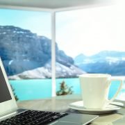 Laptop und Kaffetasse auf einem Tisch vor wunderbarer Aussicht auf See und Berge.